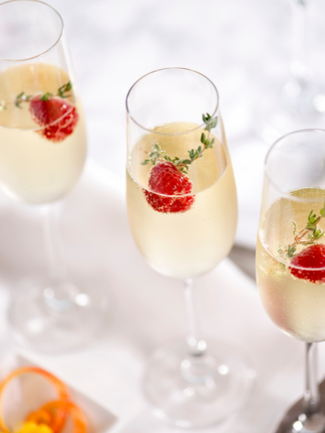 Cocktail Mangue Royale avec du champagne et de la crème de mangue décoré avec une framboise et servi dans une flûte à champagne