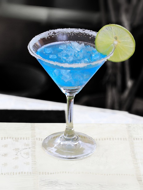 Cocktail bitter sweet caïpi de couleur bleu servi dans un verre martini avec du sucre sur les bords du verre et une rondelle de citron vert