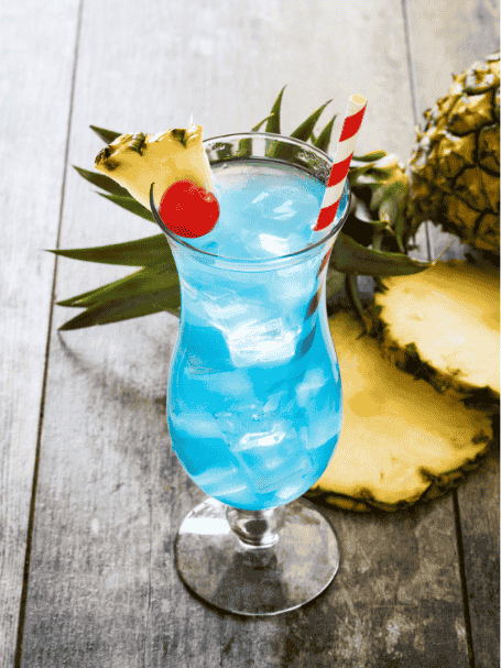 Cocktail blue hawaiian avec du rhum et du curaçao bleu, servi dans un verre décoré avec une cerise confite et de l'ananas