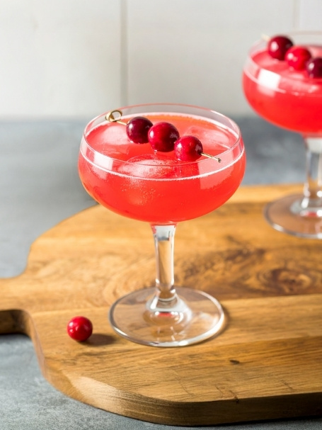 Mocktail à base de pétillant sans alcool, de jus de cranberry, de sirop de citron et de sirop de cassis, dans un verre à cocktail avec des glaçons.