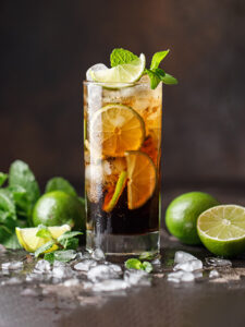 cocktail cuba libre à base de rhum citron vert avec des glaçons, des citrons verts et de la menthe servi dans un verre long drink