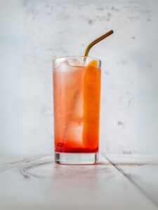 Cocktail Dream Fizz orange avec gin, sirop de framboise, jus de citron vert pressé et eau gazeuse vservi dans un verre long drink avec des glaçons