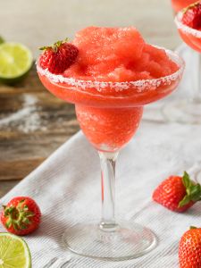 Cocktail frozen Strawberry Margarita dans un verre à margarita givré avec du sel et décoré d'une fraise.