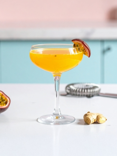 Cocktail à base de Vodka, de jus de maracujà, de jus d'abricot et de gingembre, dans un verre à cocktail avec une tranche de fruit de la passion.