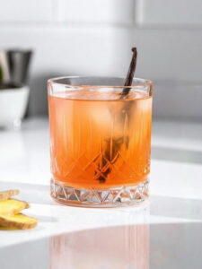 Cocktail Ginger Punch dans un verre old fashioned, à base de Rhum ambré Saint James, de jus de citron vert pressé, de jus de pamplemousse, de sirop de canne Canadou et de gingembre, avec des glaçons et de la vanille en décoration.