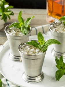 cocktail mint julep à base de bourbon, de sirop de canne et de menthe, servi dans un verre en cuivre posé sur une assiette.
