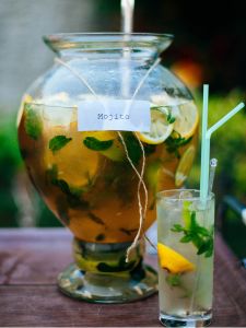 Pichet du cocktail MOjito avec rhum citron vert et menthe, à côté d'un verre avec un mojito