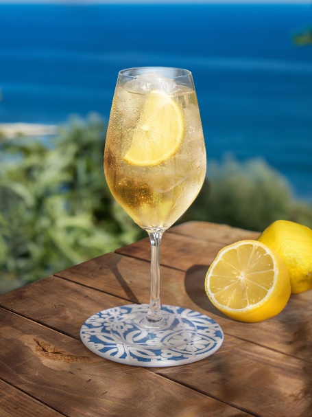 Cocktail Porto Tonic, dans un verre à vin et garni d'un quartier de citron jaune.