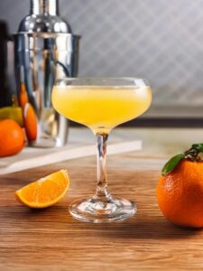 cocktail sour clyde servi dans une coupe posé sur une table en bois dans une cuisine lumineuse