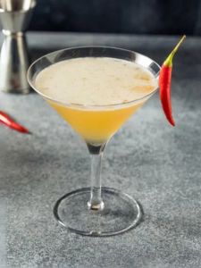 Cocktail avec des épices et du miel, de la vodka aromatisée à la vanille, de la fleur de sureau servi dans un verre décoré avec un piment rouge