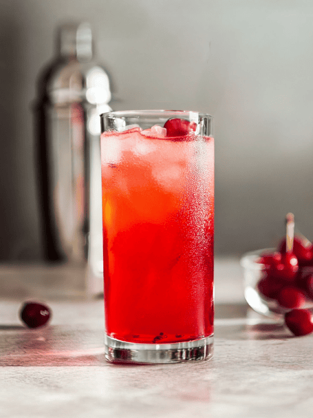 Cocktail au Porto blanc et liqueur de cerise servi dans un verre long drink décoré avec une cerise.