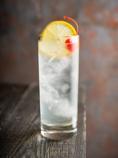 Cocktail Tom Collins avec gin et eau gazeuse servi dans un verre décoré avec du citron jaune et une cerise