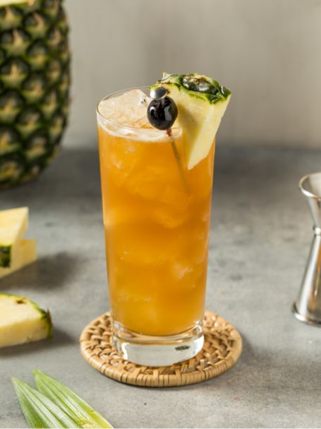 Cocktail avec du rhum ambré et jus de goyave et jus d'ananas dans un verre décoré avec un petit morceau d'ananas