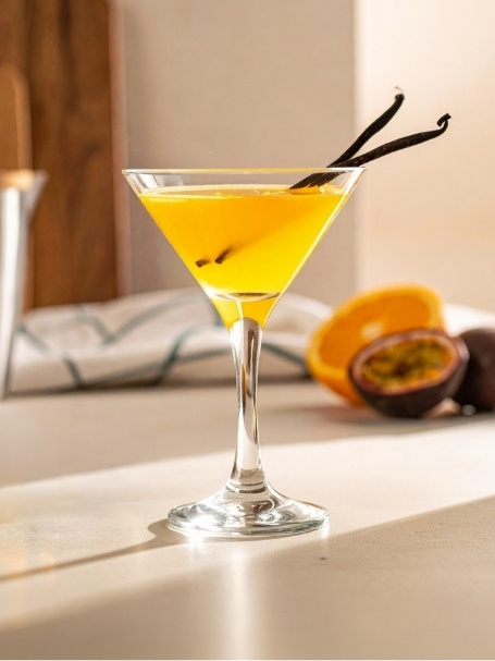 Cocktail Vanillaska dans un verre à cocktail, à base de Vodka Poliakov, de nectar de maracujà Caraïbos, de sirop de canne Canadou, de jus d'orange, d'une pincée Vanille, de jus de citron vert pressé, d'un demi fruit de la passion et de citronnelle.