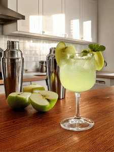 Verre à cocktail contenant un English Garden avec gin, liqueur de pomme et garniture de tranches de pomme verte.
