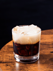 Cocktail White Russian dans un verre à rocks, composé de vodka, liqueur de café et crème, servi avec des glaçons.