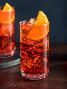 Cocktail Americano dans un verre long drink, à base de bitter rouge, de vermouth rouge et d'eau gazeuse, avec des glaçons et une tranche d'orange dans le verre.
