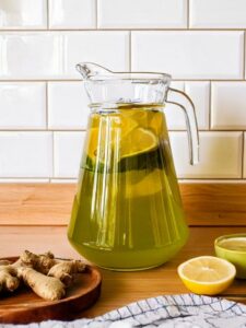 Cocktail Green Tea Punch dans une carafe avec du citron jaune, du thé et du gingembre dans une cuisine
