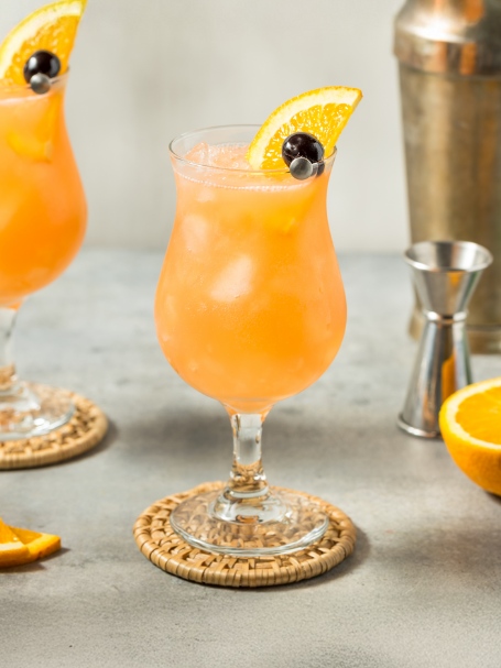 Cocktail Hurricane, servi dans un verre tulipe et décoré d'une brochette avec cerise confite et quartier d'orange.
