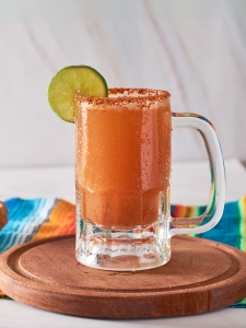 Cocktail mexicain Michelada avec de la bière complétée par du jus de citron vert, du sel et une sauce piquante servi dans un verre avec les bords salés.