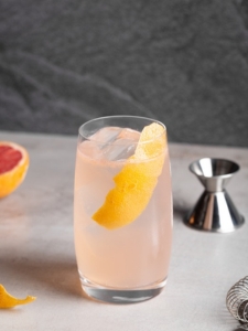 Cocktail Paloma avec de la Tequila et du soda au pamplemousse servi dans un verre décoré avec un zeste d'orange et des glaçons.