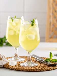 Cocktail au gin tonic et au thé vert avec du miel servi dans un verre avec des glaçons et décoré avec quelques feuilles de menthe.