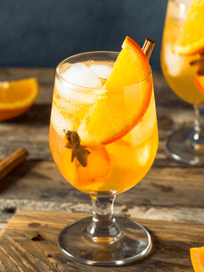 Cocktail Punch au thé fumé avec rhum ambré, jus d’ananas, épices servi dans un verre avec des glaçons et tranche d'orange