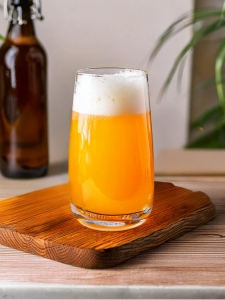 Cocktail Exotic Beer servi dans un verre sur un plna de travail en bois avec une bouteille de bière et des feuilles exotiques en arrière plan.