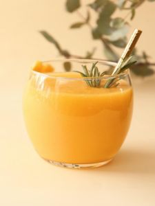ocktail Banana Kiss avec nectar de banane , nectar de mangue, nectar de maracujà et sirop de canne servi dans un verre à cocktail avec du romarin et une paille dorée