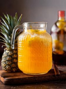 Rhum arrangé ananas de couleur jaune et orange servi dans une vasque sur une table en bois