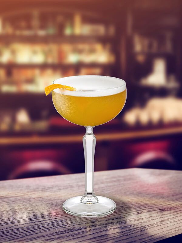 Cocktail sour clyde dans un verre à pied avec de la glace et des zestes d'orange