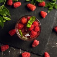 Cocktail à base de framboise servi dans un verre avec des glaçons et des fruits frais
