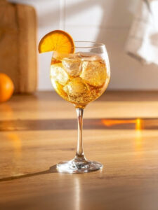 Cocktail St Raph Tonic dans un verre piscine, à base de Saint Raphael ambré, de tonic et d'un quartier d' orange, avec des glaçons.