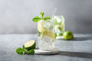 cocktail mojito servi dans un verre long drink avec du citron vert et de la menthe dans un décor uni gris