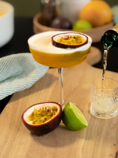 Cocktail Pornstar Martini à base de vodka, de nectar de maracujà, de sirop de vanille, de liqueur de fruit de la passion et jus de citron vert, dans un verre à cocktail avec un fruit de la passion en décoration.