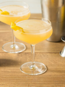 Cocktail Corpse Reviver 2, à base de gin, de triple sec et de vermouth servi dans un verre à cocktail et décoré d'un zeste de citron.