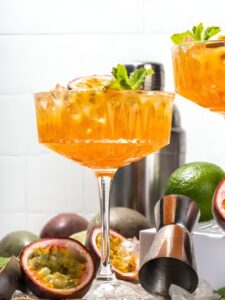 Cocktail Porn Star Martini, dans un verre à cocktail, décoré d'un demi fruit de la passion et accompagné d'un shot de Prosecco avec des fruits de la passion et du citron vert dans le décor