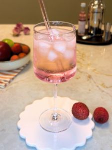 Spritz Litchi, servi dans un verre à vin, avec une paille rose en verre.