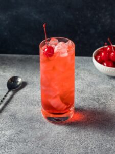 cocktail sans alcool Shirley Temple, à base de ginger ale, limonade et sirop de grenadine de couleur rose et rouge avec une cerise sur le dessus