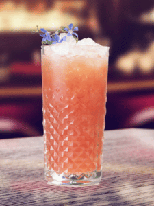 Cocktail Fleur de lotus sans alcool à l'ananas, jus de framboise, de Litchi et sirop de fleur de sureau servi dans un verre décoré avec une fleur comestible.
