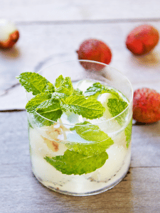 Mojito au litchi garni de feuilles de menthe et de morceaux de litchi, servi dans un verre avec des glaçons