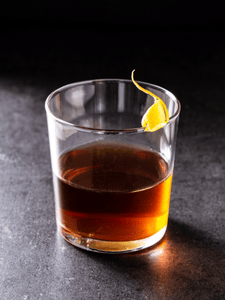 Cocktail Sazerac avec du cognac, de sucre, du bitter et de l'absinthe, servi dans un verre décoré avec un zeste de citron