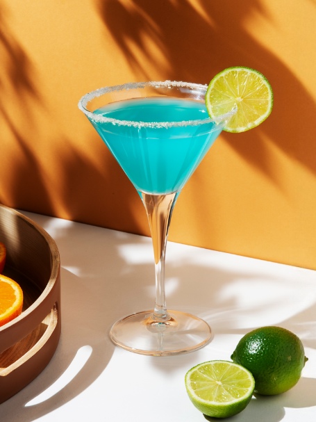 cocktail blue margarita de couleur bleu vif servi dans un verre martini avec du sel sur le bord du verre et une rondelle de citron vert