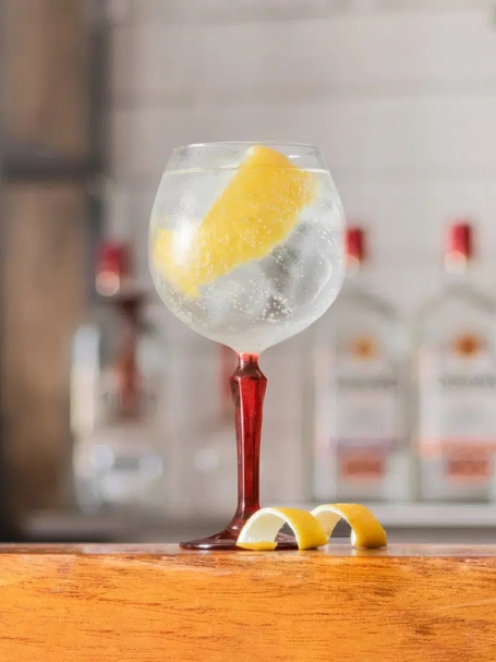 Cocktail gin tonic servi dans un verre à pied, préparé avec du gin, du tonic et garni d'un zeste de citron jaune posé sur un comptoir de cuisine