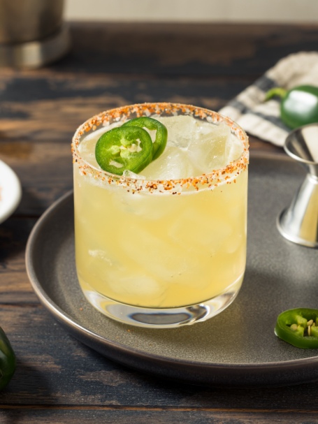 Cocktail Spicy Margarita, servi dans un verre old fashioned décoré de tranches de jalapeno et givré de poudre de piment rouge.