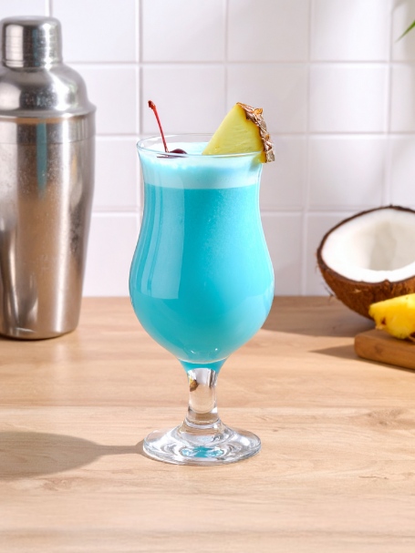 cocktail swimming pool de couleur bleu avec une texture crémeuse et veloutée. Le cocktail est ornée d'un quartier d'ananas et d'une cerise confite sur le dessus