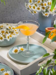 Cocktail orange dans un verre à martini et décoré d'un zeste d'orange.