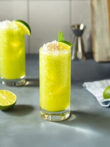 cocktail chartreuse swizzle dans un verre long drink de couleur jaune et vert avec de la noix de muscade et de la glace pilée sur le dessus
