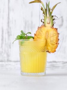 Cocktail Pisco Punch, dans un verre old fashioned et décoré de feuilles de menthe et d'un mini ananas.