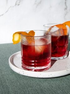 cocktail rabo de galo de couleur rouge foncé dans un verre old fashioned avec un zeste d'orange